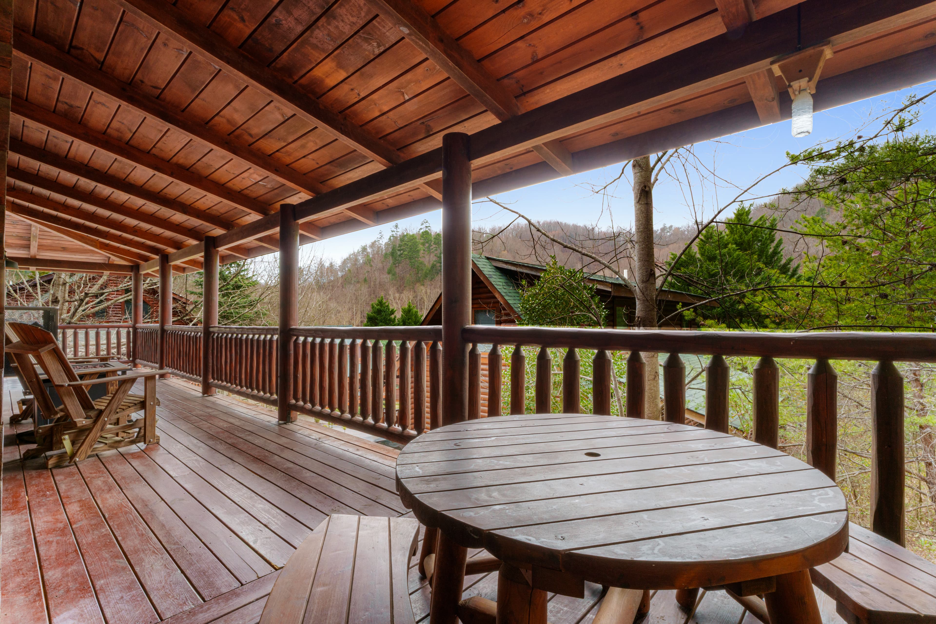 Rustic wooden deck featuring a round table and benches overlooking a scenic forest view.