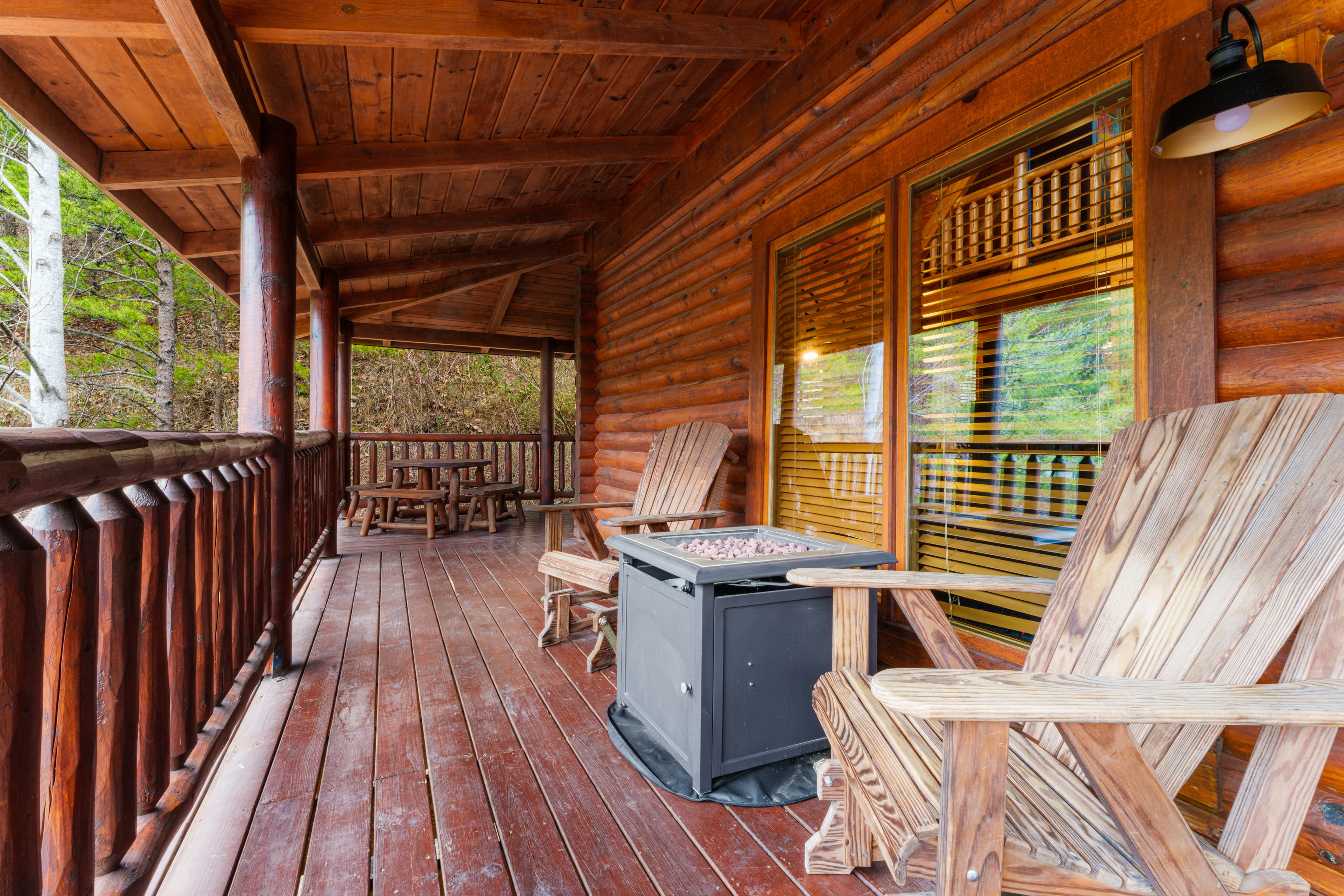 Rustic log cabin porch featuring wooden Adirondack chairs, a fire pit, and forest views.