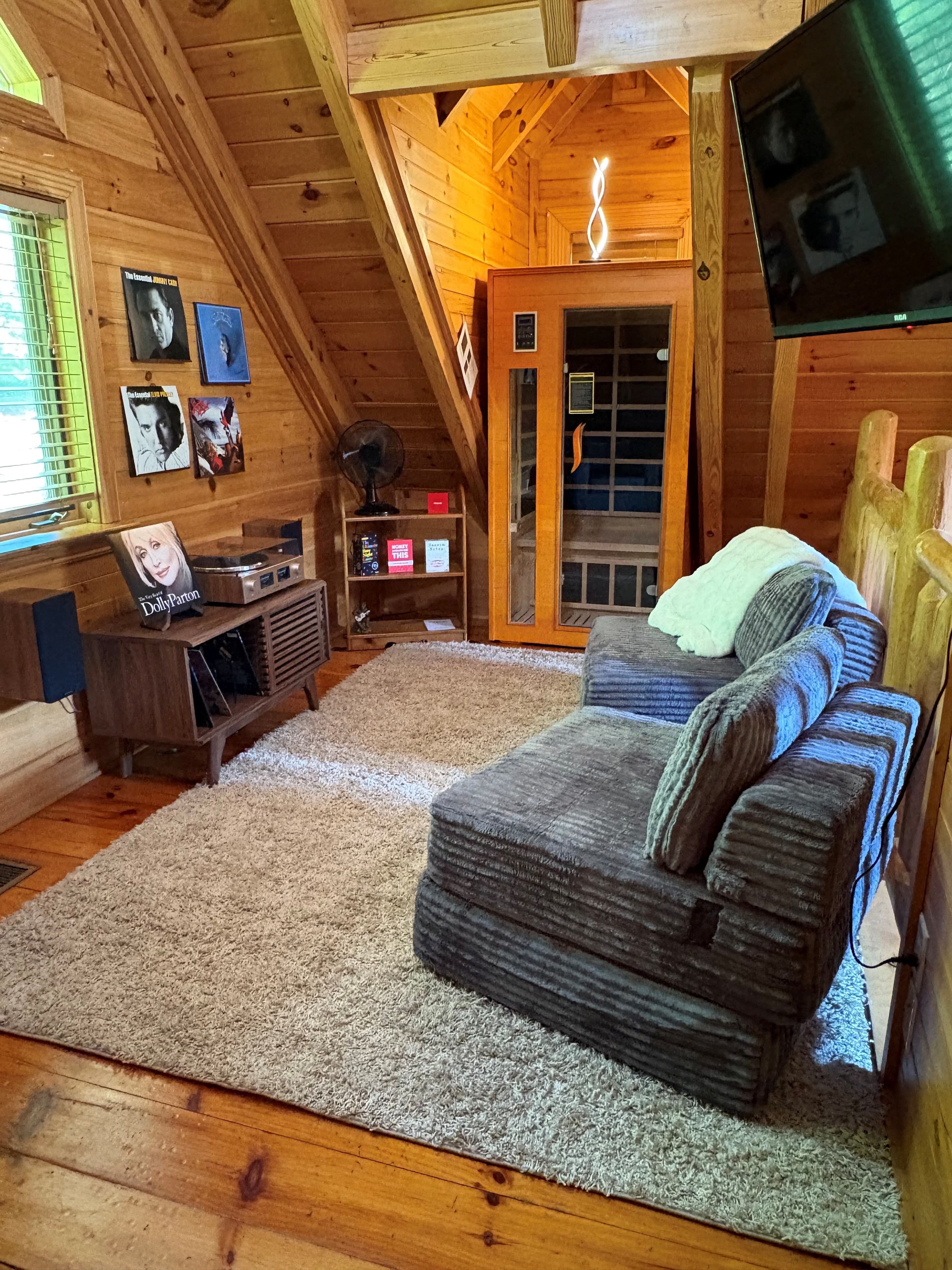 Cozy wood-paneled room with a grey sofa, record player, and a small indoor sauna.